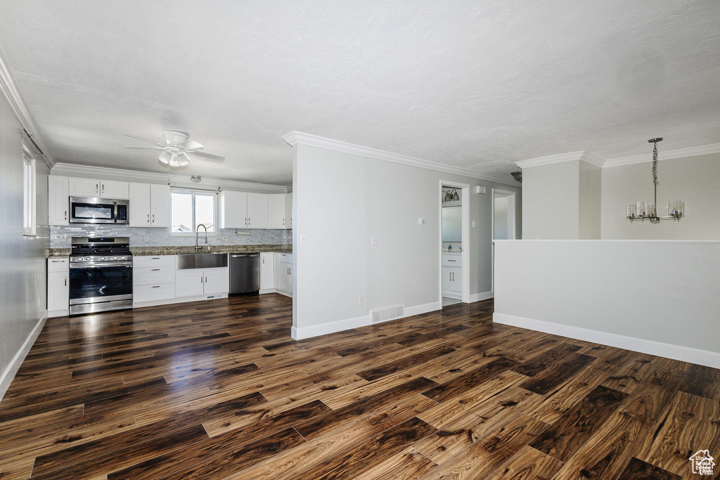 Unfurnished living room with dark wood finished floors, a ceiling fan, crown molding, a chandelier, and baseboards