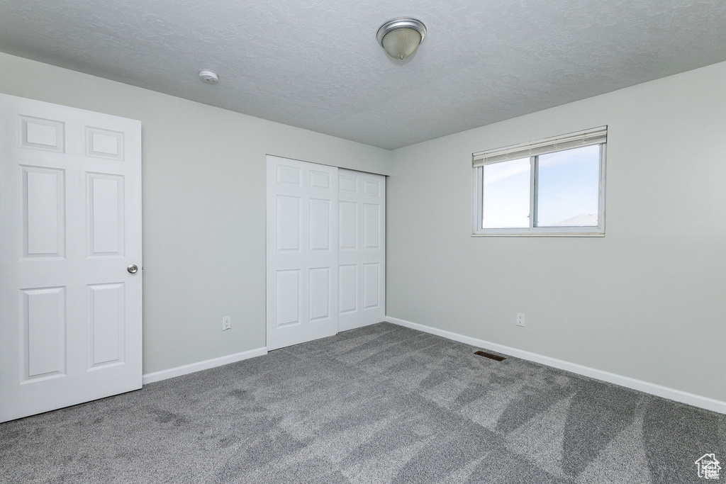 Unfurnished bedroom featuring carpet, baseboards, a closet, and a textured ceiling