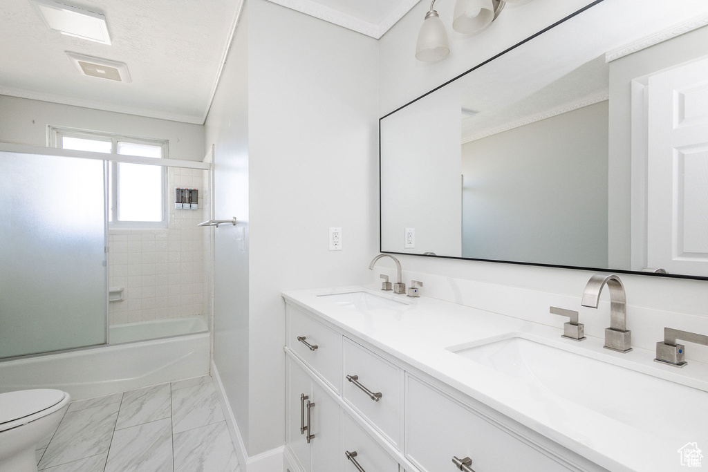 Bathroom with marble finish flooring, toilet, double vanity, baseboards, and bath / shower combo with glass door
