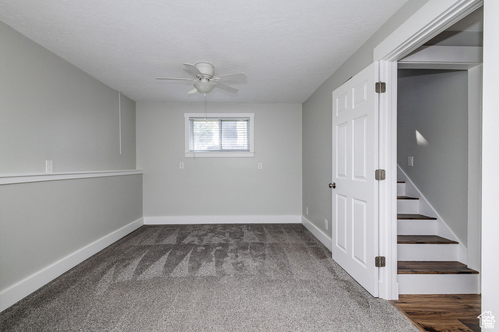 Unfurnished room featuring a ceiling fan, dark colored carpet, baseboards, and stairway