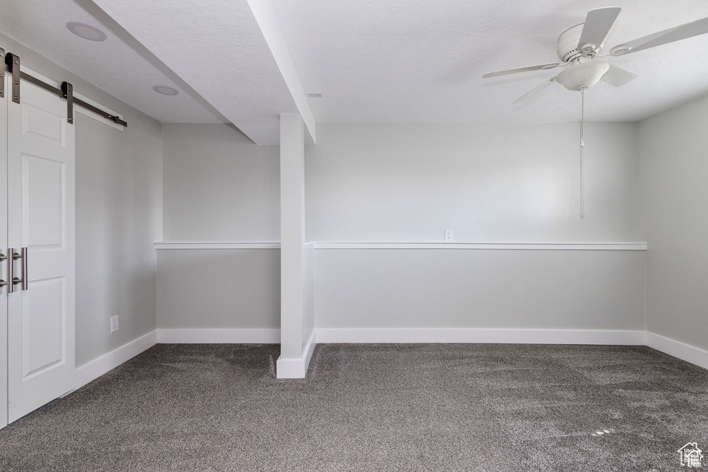 Empty room with carpet floors, a barn door, a ceiling fan, and baseboards
