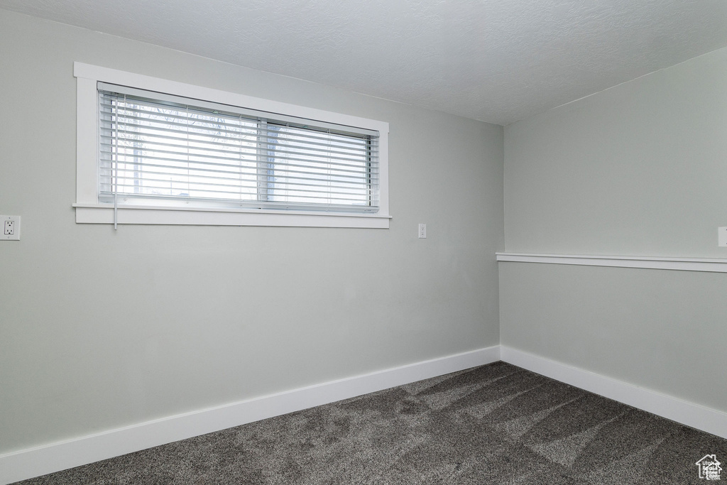 Unfurnished room with dark carpet, baseboards, and a textured ceiling