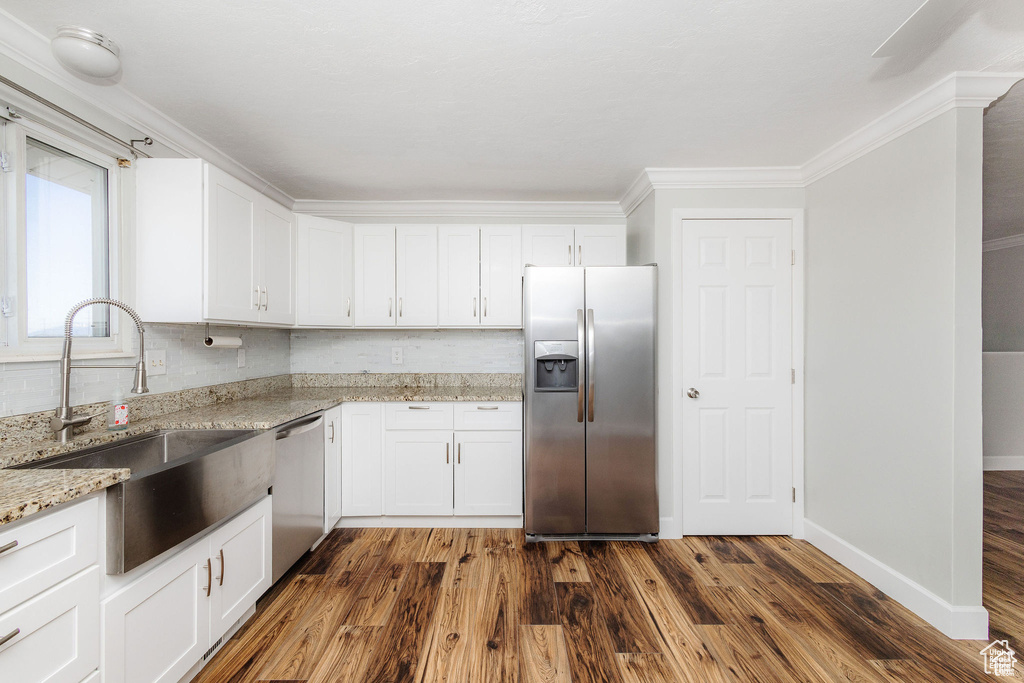 Kitchen with stainless steel appliances, a sink, crown molding, light stone counters, and dark wood-style flooring