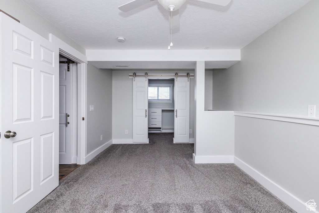 Spare room featuring carpet, a barn door, baseboards, a textured ceiling, and a ceiling fan