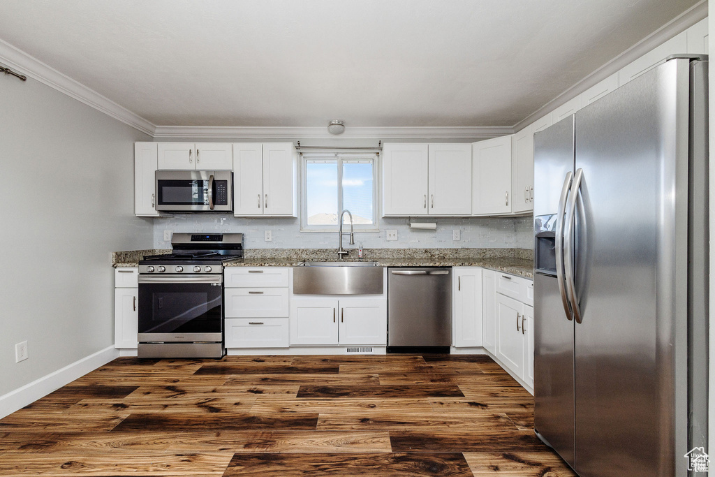 Kitchen with appliances with stainless steel finishes, ornamental molding, a sink, white cabinets, and light stone countertops