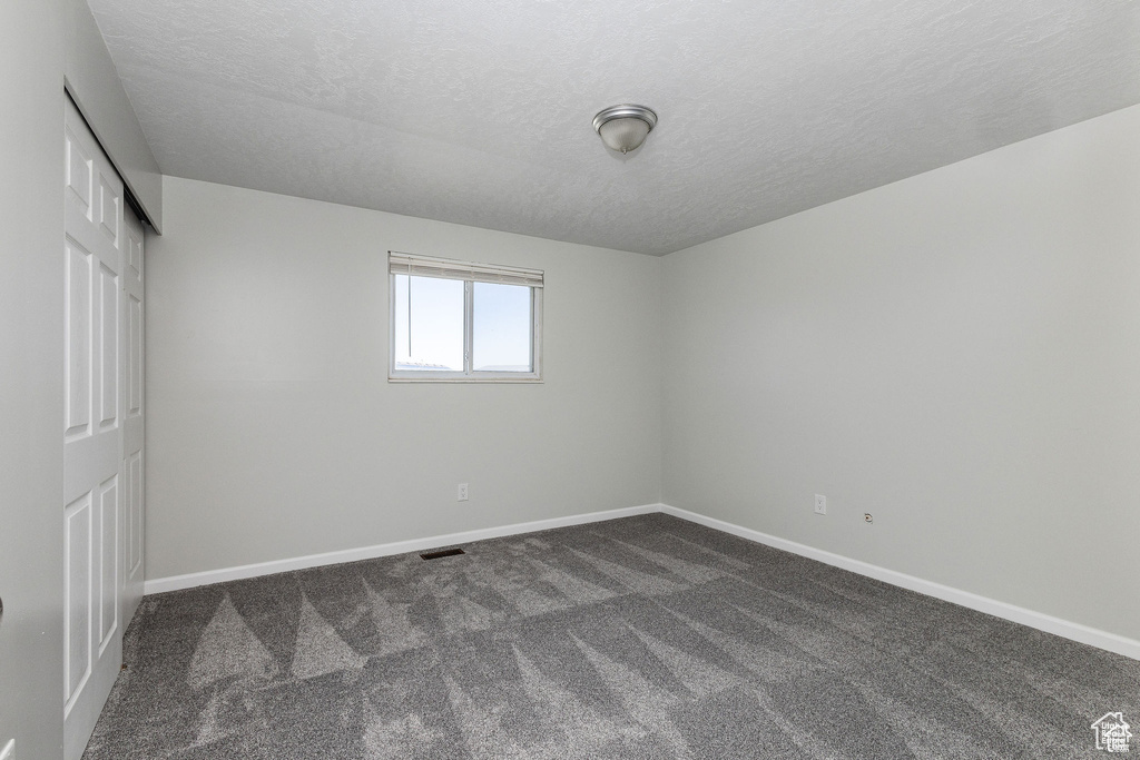 Unfurnished bedroom featuring dark carpet, a textured ceiling, baseboards, and a closet