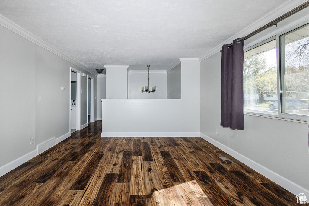 Empty room with a chandelier, crown molding, wood finished floors, and baseboards