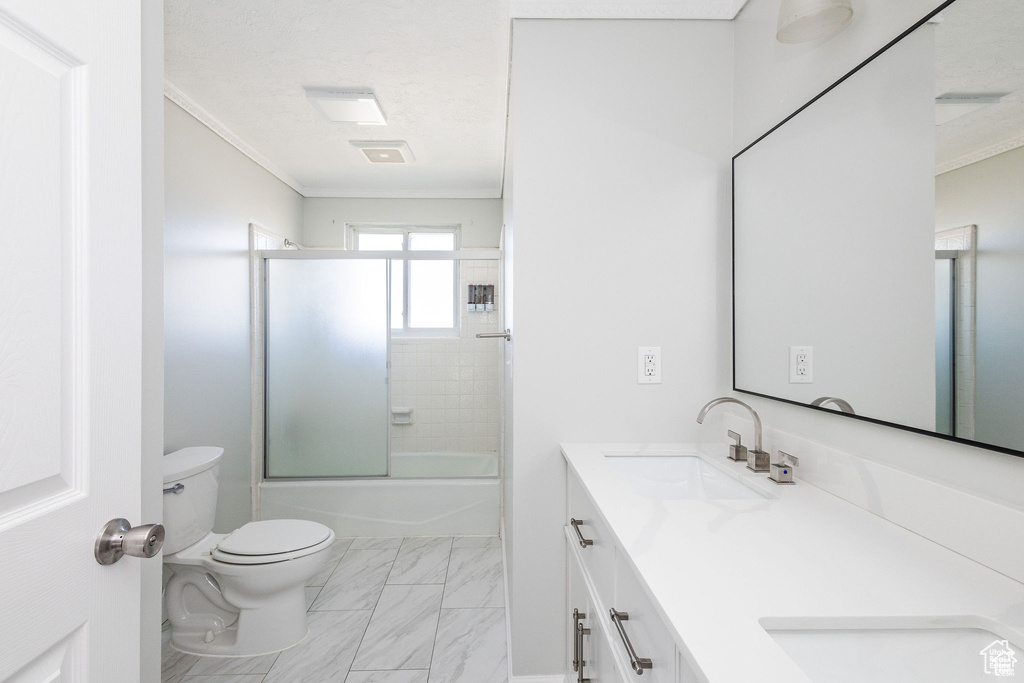Bathroom featuring ornamental molding, toilet, double vanity, marble look tile flooring, and enclosed tub / shower combo