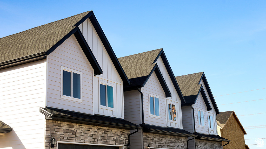 View of home\'s exterior with roof with shingles, an attached garage, stone siding, and board and batten siding