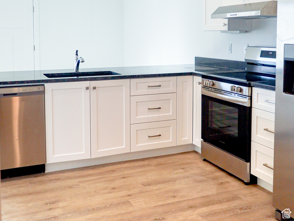 Kitchen featuring a sink, appliances with stainless steel finishes, wall chimney range hood, and white cabinetry