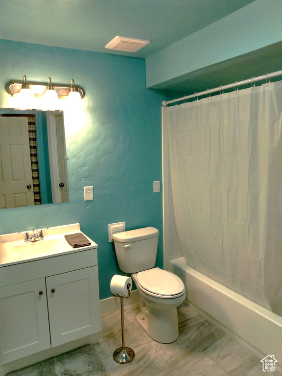 Bathroom with toilet, shower / tub combo with curtain, vanity, and a textured wall