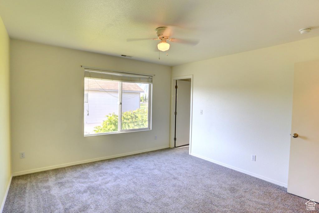 Carpeted empty room featuring ceiling fan, baseboards, and a smoke detector