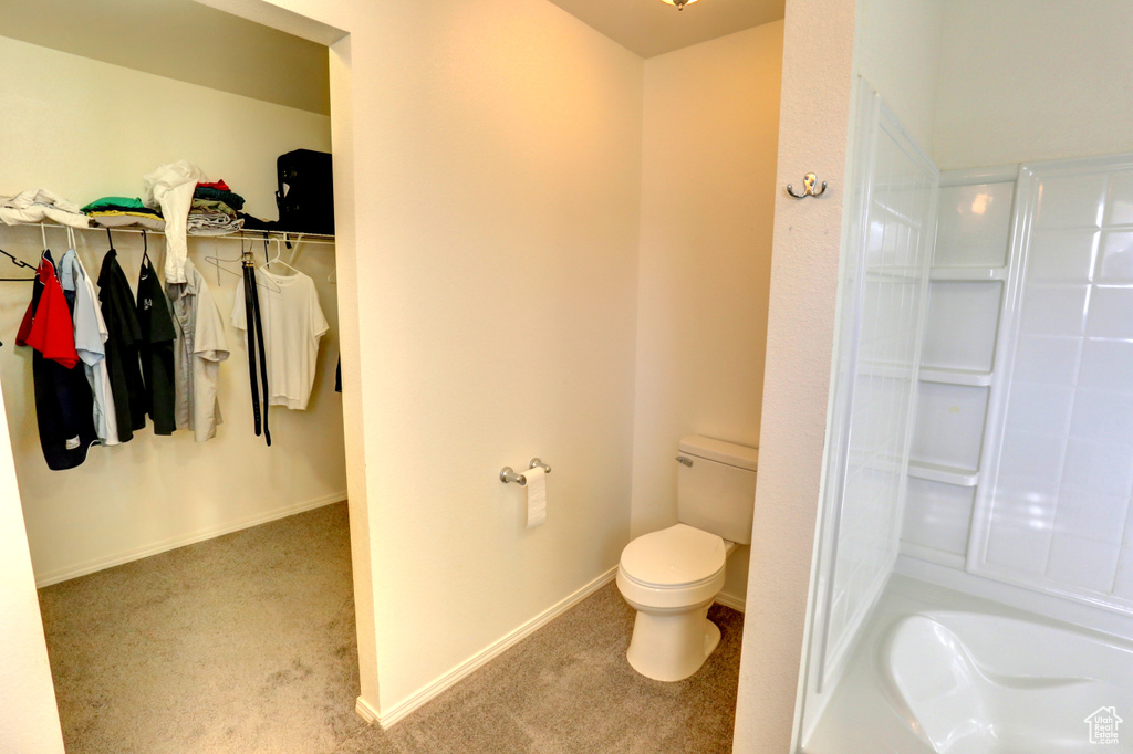 Bathroom featuring toilet, a tub to relax in, a spacious closet, and baseboards