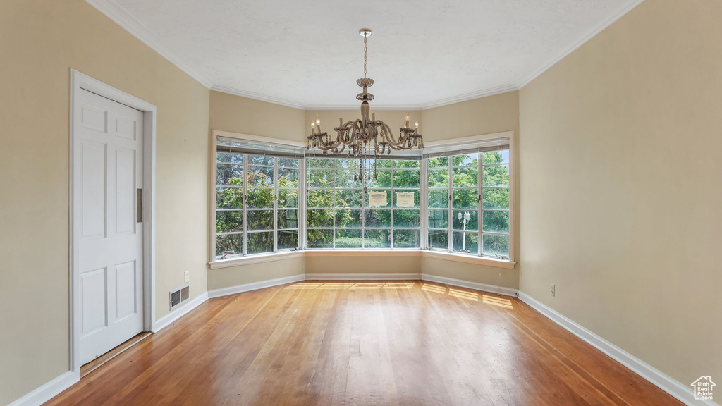 Unfurnished dining area with a chandelier, wood finished floors, plenty of natural light, and ornamental molding