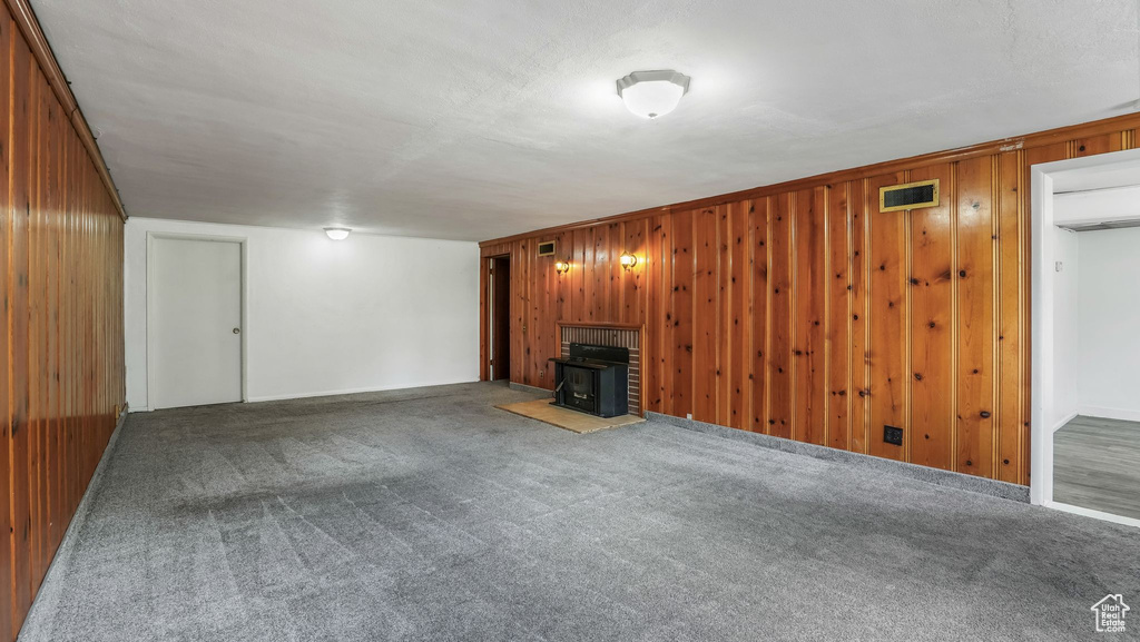 Unfurnished living room with a wood stove, wooden walls, and carpet flooring