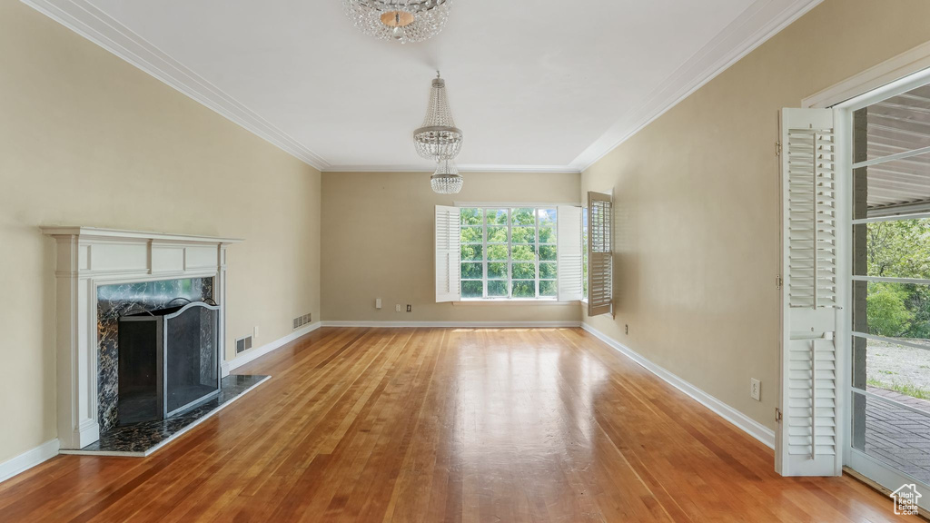 Unfurnished living room with a chandelier, wood finished floors, healthy amount of natural light, and crown molding