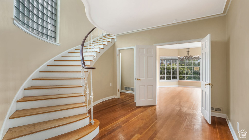 Stairway featuring wood-type flooring, a chandelier, baseboards, and ornamental molding