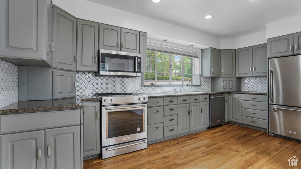 Kitchen with stainless steel appliances, gray cabinetry, a sink, dark stone counters, and light wood finished floors