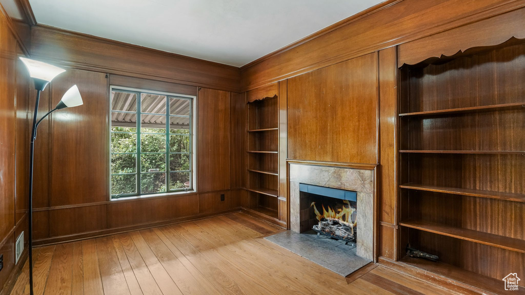 Unfurnished living room featuring a fireplace, wood-type flooring, wood walls, and built in shelves
