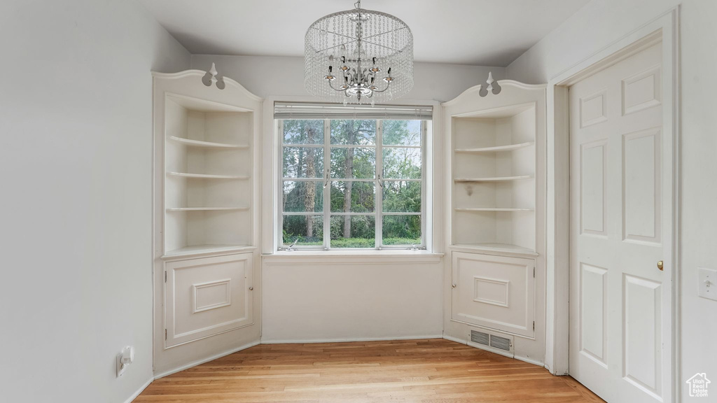 Unfurnished dining area with a chandelier, light wood-style flooring, and baseboards