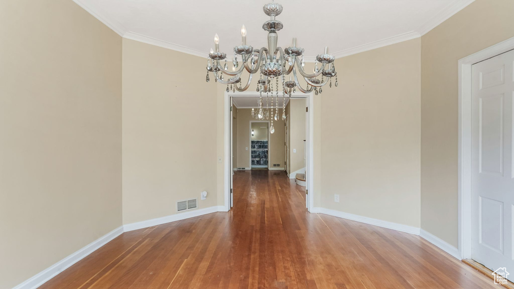 Unfurnished dining area with a chandelier, ornamental molding, wood finished floors, and baseboards
