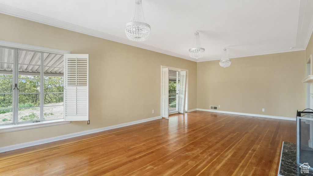 Unfurnished living room with a chandelier, healthy amount of natural light, baseboards, wood finished floors, and ornamental molding
