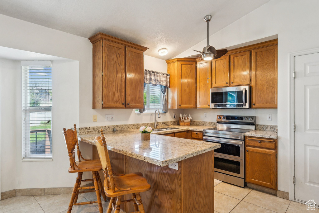 Kitchen featuring stainless steel appliances, a sink, light tile patterned floors, a peninsula, and healthy amount of natural light