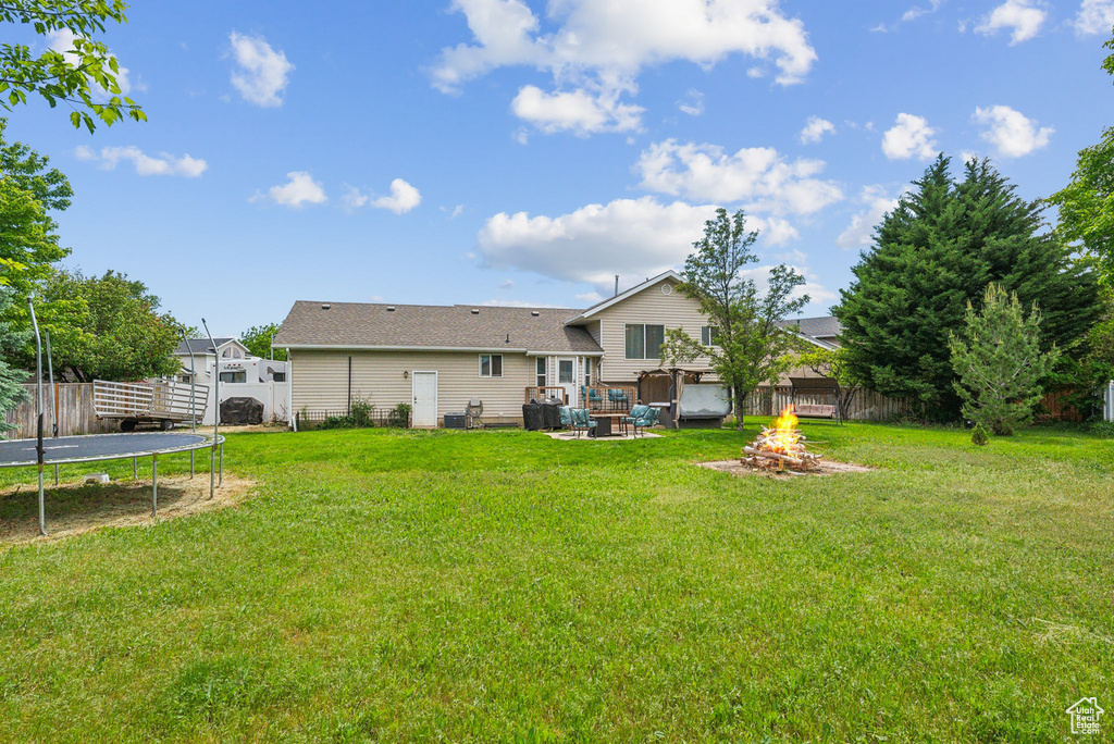 Rear view of property featuring a trampoline and a fire pit