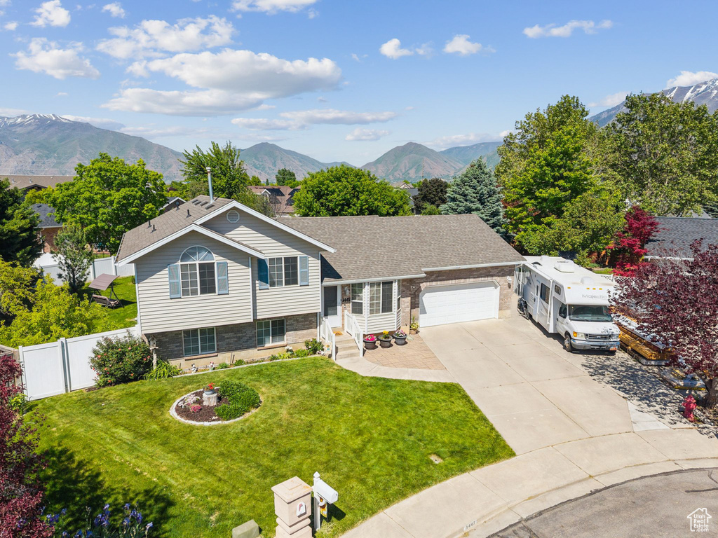 Tri-level home featuring an attached garage, driveway, a mountain view, and stone siding
