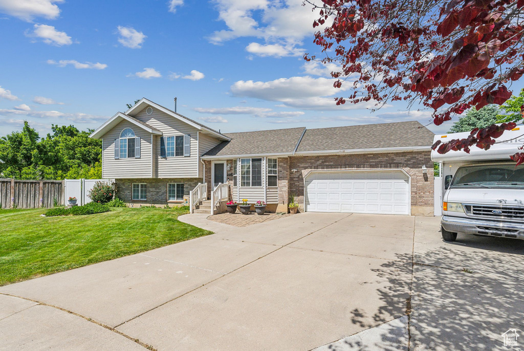 Split level home featuring brick siding, concrete driveway, an attached garage, and roof with shingles