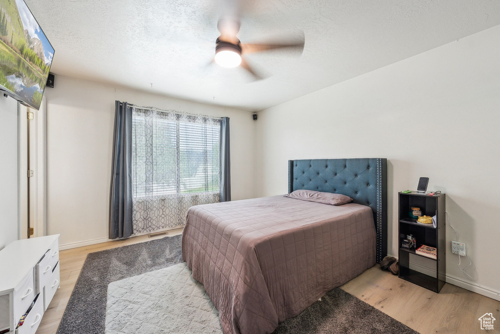 Bedroom featuring light wood-style flooring, baseboards, ceiling fan, and a textured ceiling