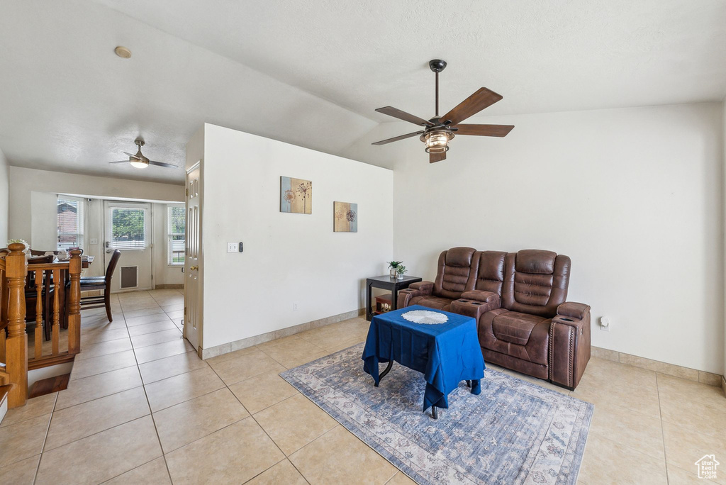 Living room featuring ceiling fan, light tile patterned floors, vaulted ceiling, and baseboards