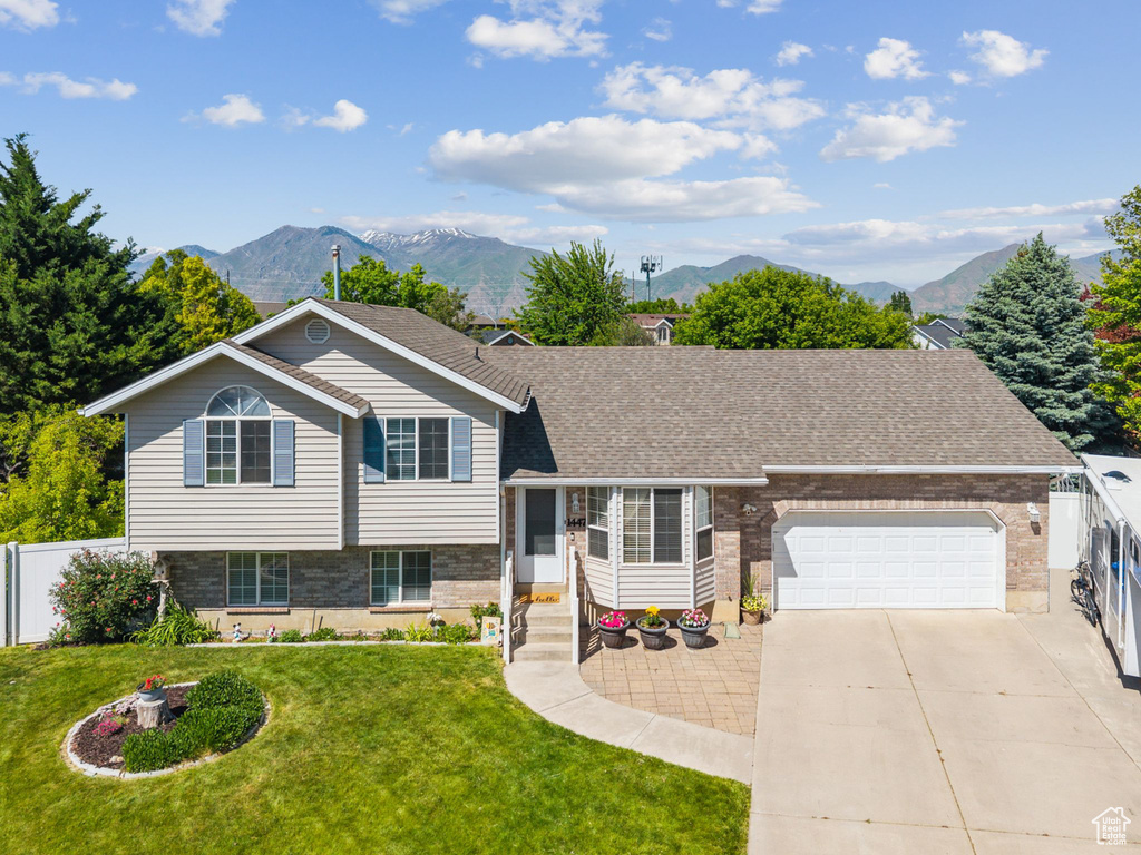 Split level home with a mountain view, an attached garage, driveway, brick siding, and a shingled roof