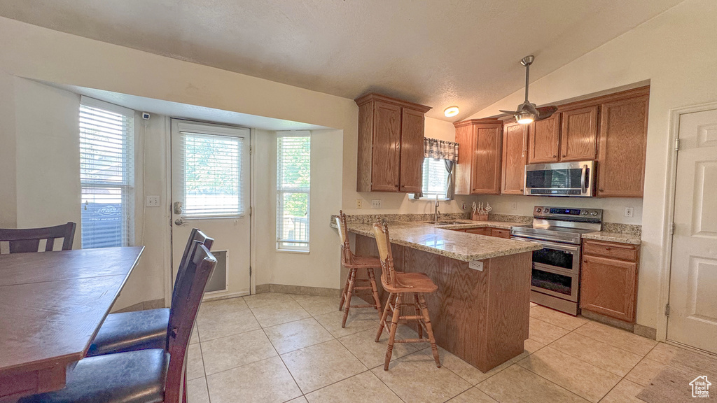 Kitchen featuring appliances with stainless steel finishes, a peninsula, light tile patterned flooring, a breakfast bar, and vaulted ceiling