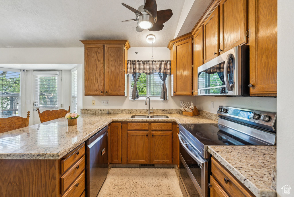 Kitchen with appliances with stainless steel finishes, a sink, a peninsula, and brown cabinetry
