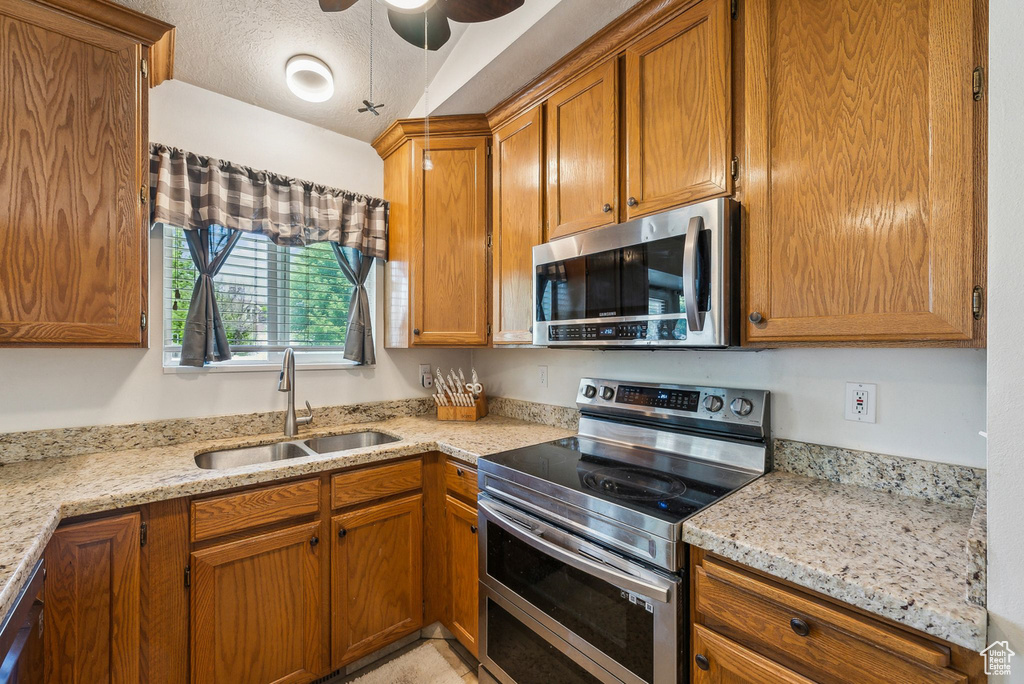 Kitchen with appliances with stainless steel finishes, a sink, a ceiling fan, light stone countertops, and a textured ceiling