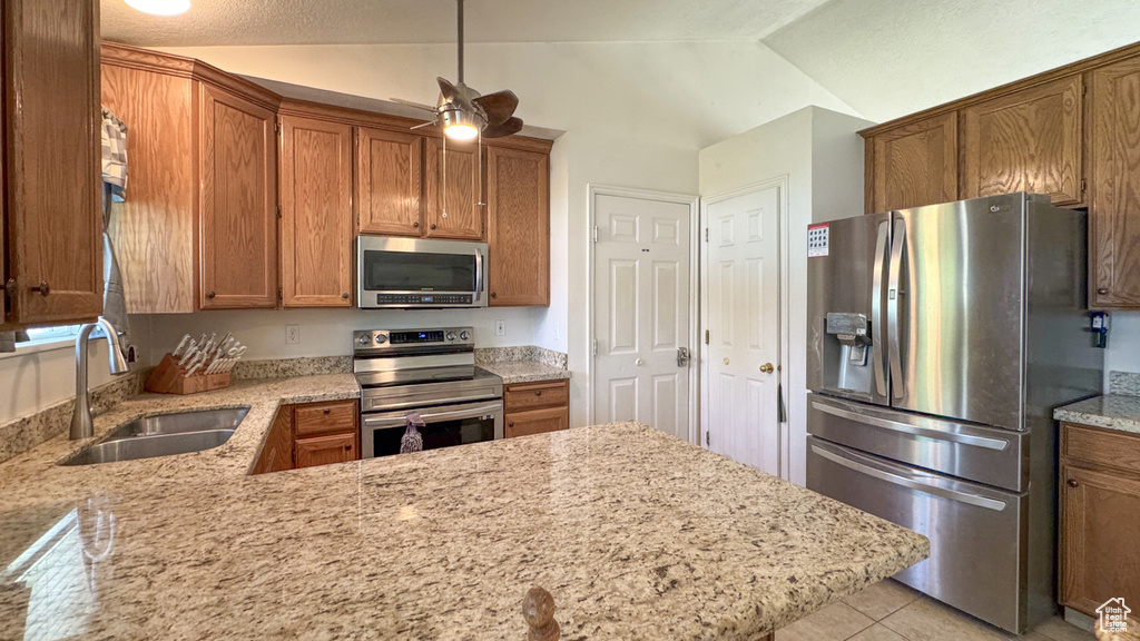 Kitchen featuring stainless steel appliances, a sink, brown cabinets, light stone counters, and lofted ceiling