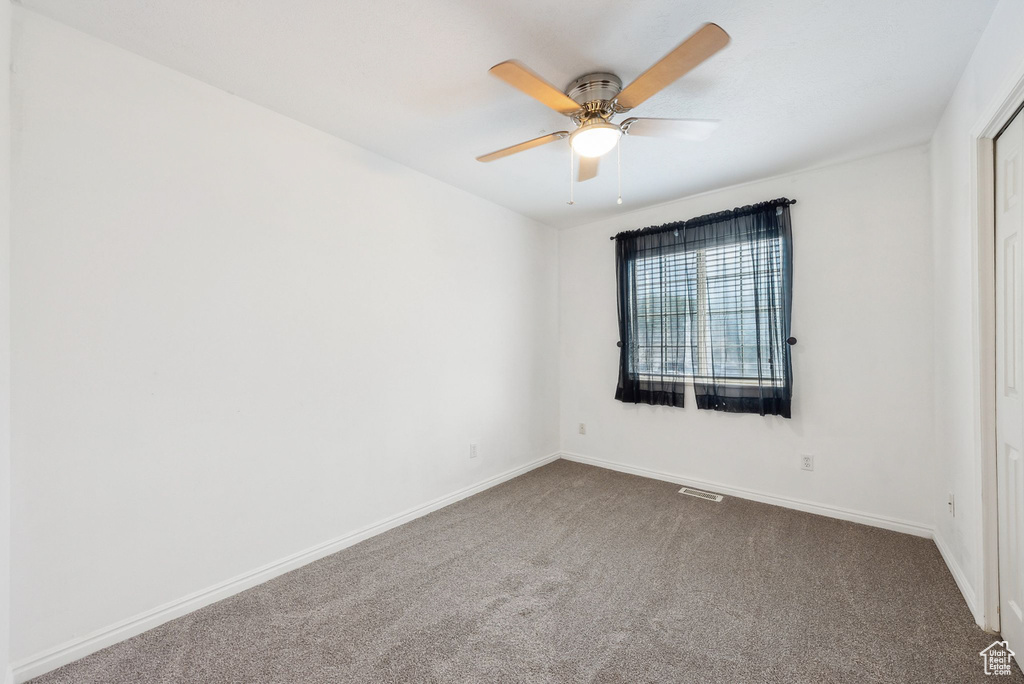 Empty room featuring dark carpet, a ceiling fan, and baseboards