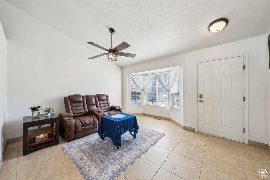 Living room featuring a ceiling fan, light tile patterned floors, baseboards, and vaulted ceiling