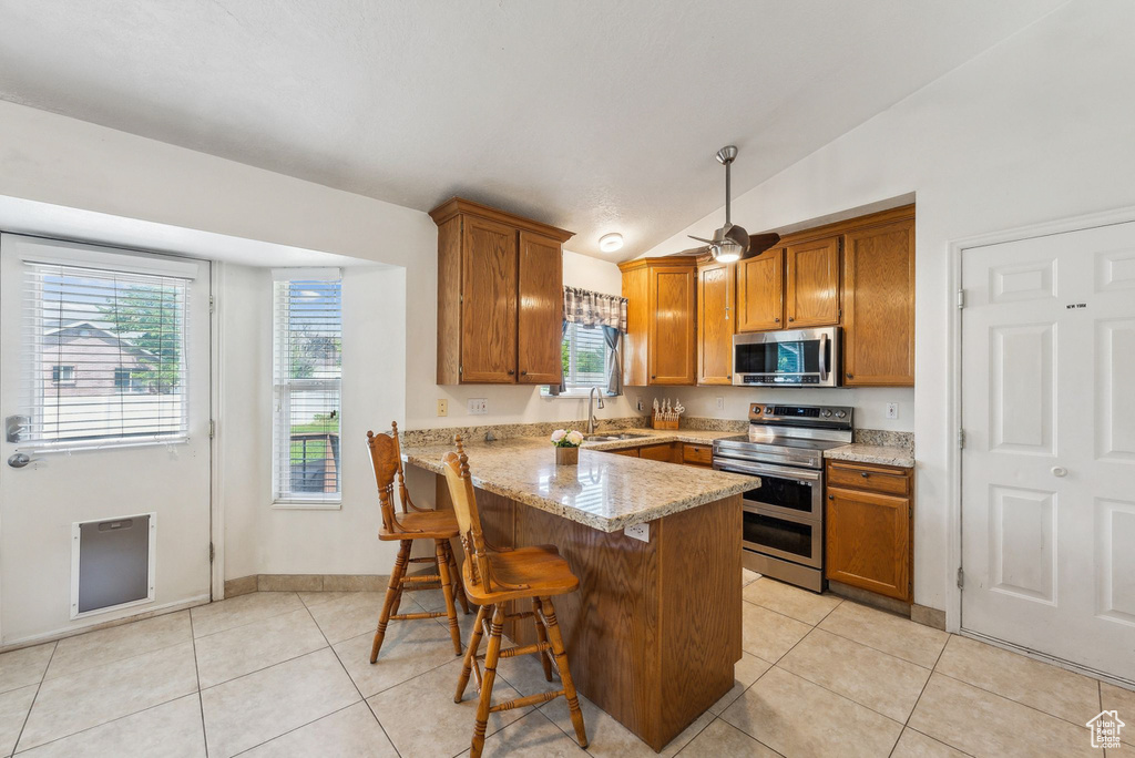 Kitchen with stainless steel appliances, brown cabinets, a sink, a peninsula, and light tile patterned flooring