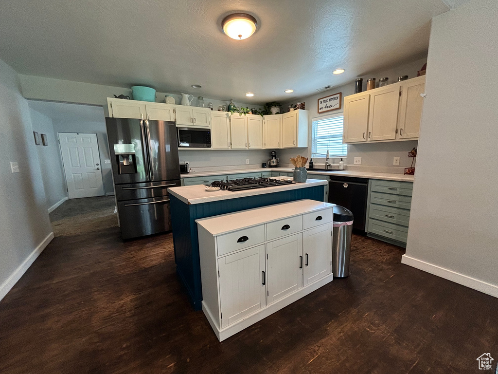 Kitchen with stainless steel appliances, a kitchen island, light countertops, baseboards, and dark wood-type flooring