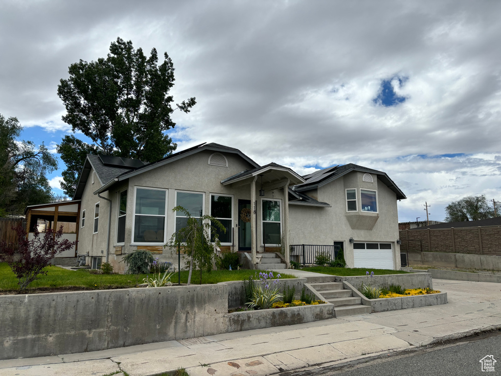 View of front of house with stucco siding, roof mounted solar panels, a garage, and fence