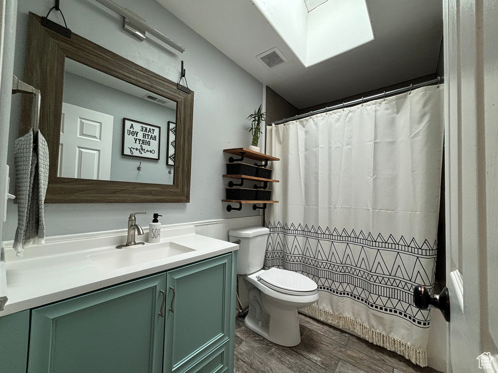 Bathroom featuring toilet, vanity, wood finished floors, and a skylight