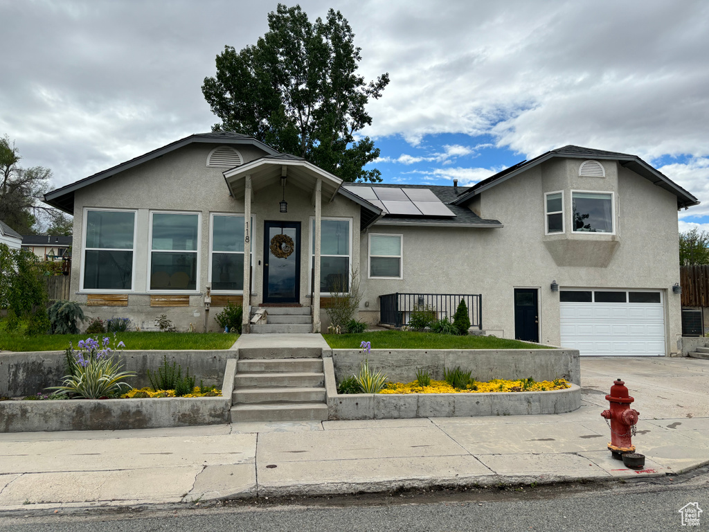 View of front of home with stucco siding, a garage, roof mounted solar panels, and concrete driveway