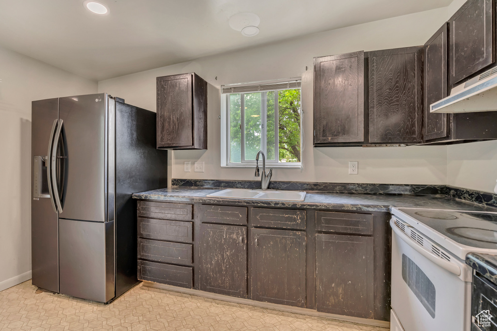 Kitchen featuring stainless steel refrigerator with ice dispenser, white range with electric stovetop, a sink, dark brown cabinets, and recessed lighting