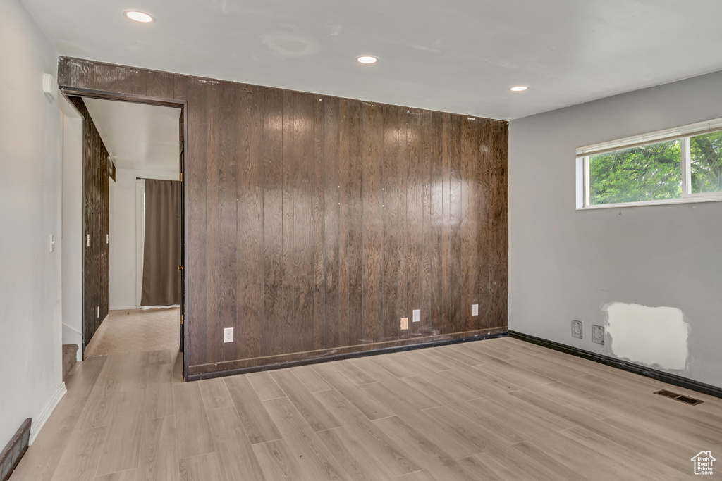 Empty room with light wood finished floors, recessed lighting, wood walls, and baseboards