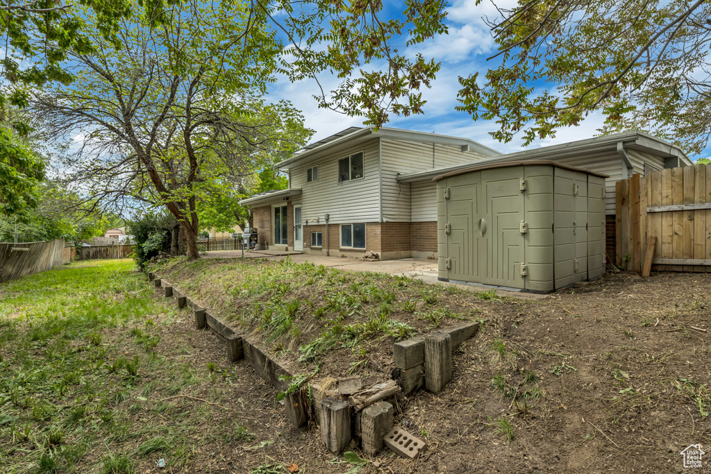 Rear view of house with brick siding, a patio area, fence, and a shed