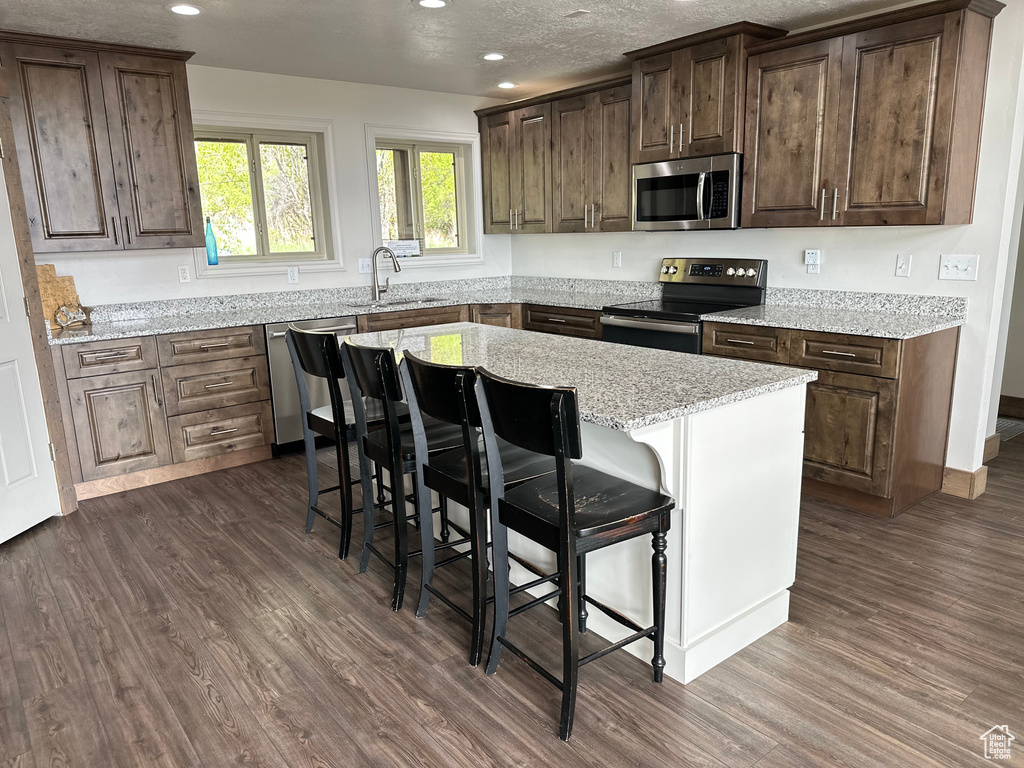 Kitchen featuring appliances with stainless steel finishes, a sink, dark wood-style floors, recessed lighting, and a kitchen bar