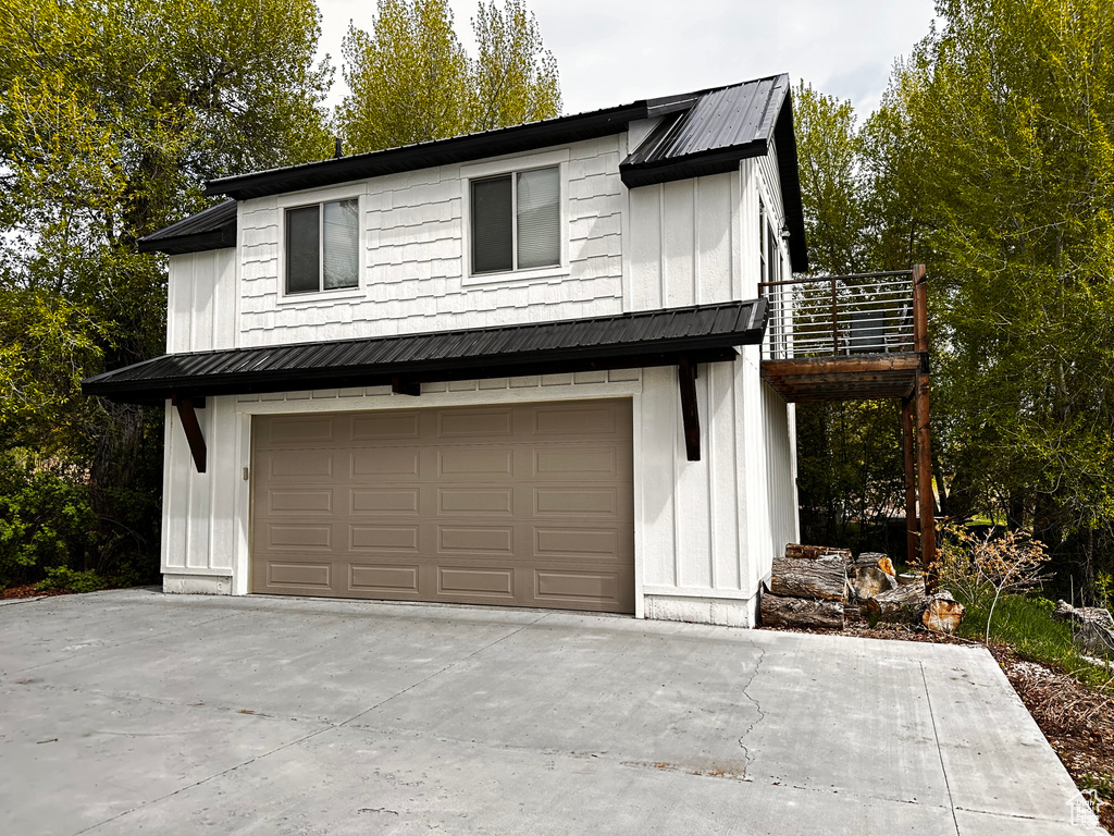 Modern farmhouse style home featuring board and batten siding, an attached garage, metal roof, and driveway