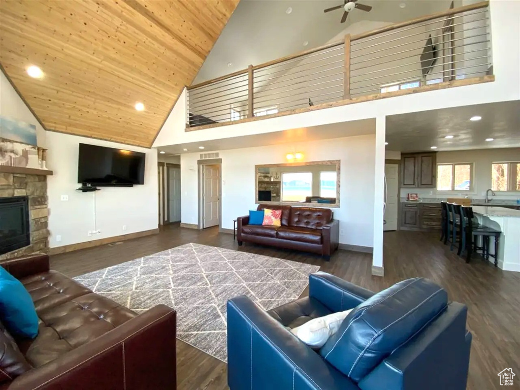 Living area with high vaulted ceiling, a ceiling fan, wood ceiling, a fireplace, and dark wood finished floors